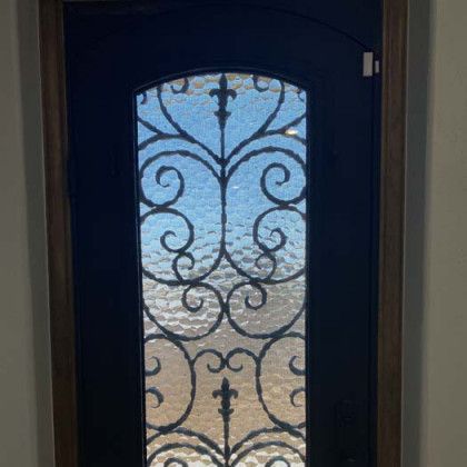 Black front door with decorative ironwork and textured glass.