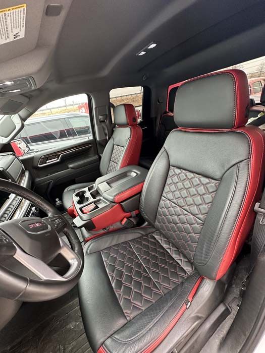 Black and red leather interior of a GMC truck. Seats have diamond stitching and red accents.