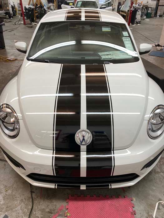 White Volkswagen Beetle with black racing stripes in a garage.