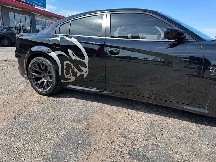 Black Dodge Charger with a silver Hellcat decal parked on asphalt.