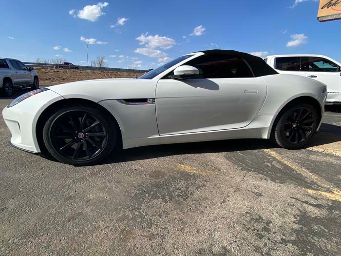 White Jaguar F-Type convertible with black wheels parked on asphalt on a sunny day.