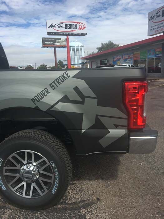 Black pickup truck with Power Stroke graphics. Billboard, water tower, and buildings in the background.