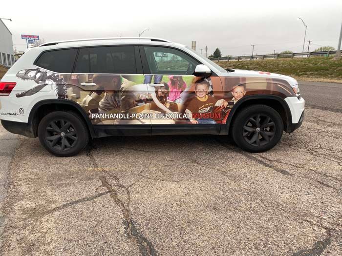 White SUV with side wrap advertising; people, dogs, and text on asphalt.