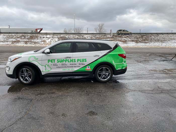 White Pet Supplies Plus SUV with green accents parked on wet pavement.