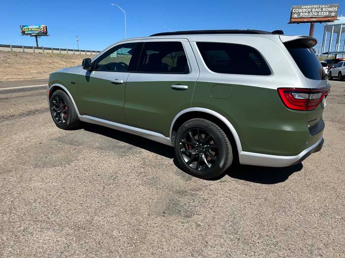 Olive green and silver SUV parked on pavement next to a highway.