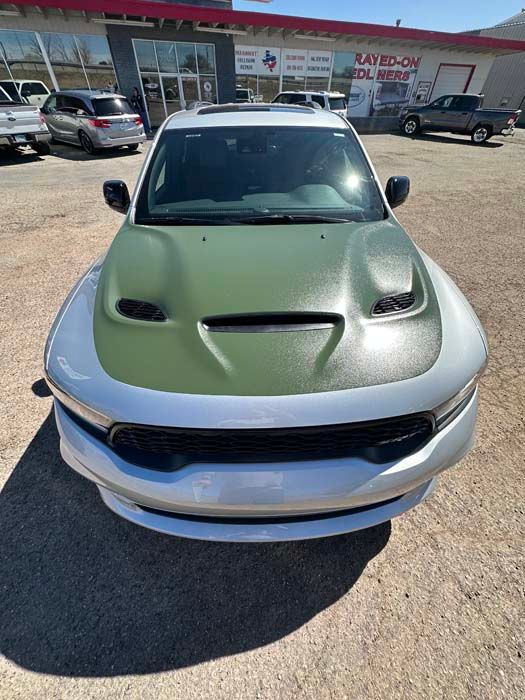 Silver Dodge Durango with a green textured hood, parked outside a building on a sunny day.