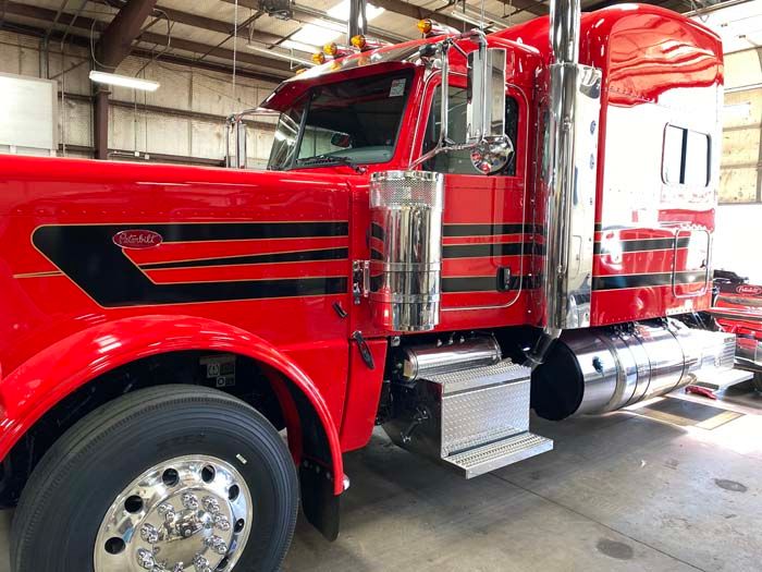 Red Peterbilt semi-truck with chrome details and black stripes parked in a garage.