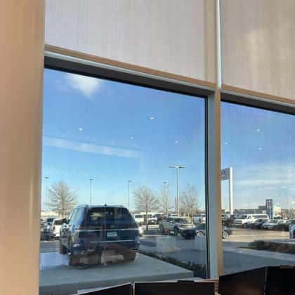 View through a window showing a car, parked lot, and blue sky.