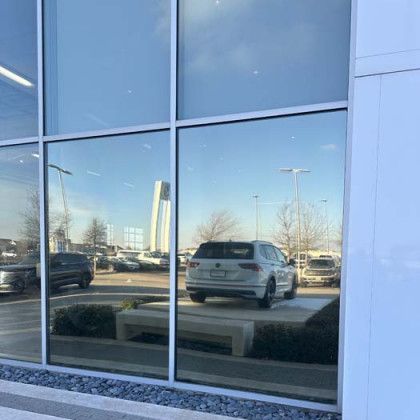 Glass windows reflecting a car dealership, with cars, trees, and a blue sky visible.