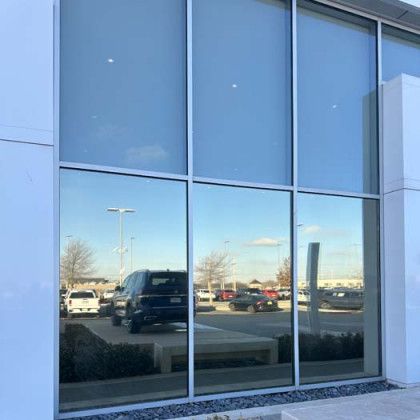 Large glass windows reflect cars parked in a lot, set against a white building.