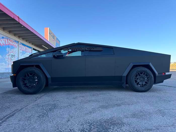 Black Tesla Cybertruck parked beside a building on a sunny day.