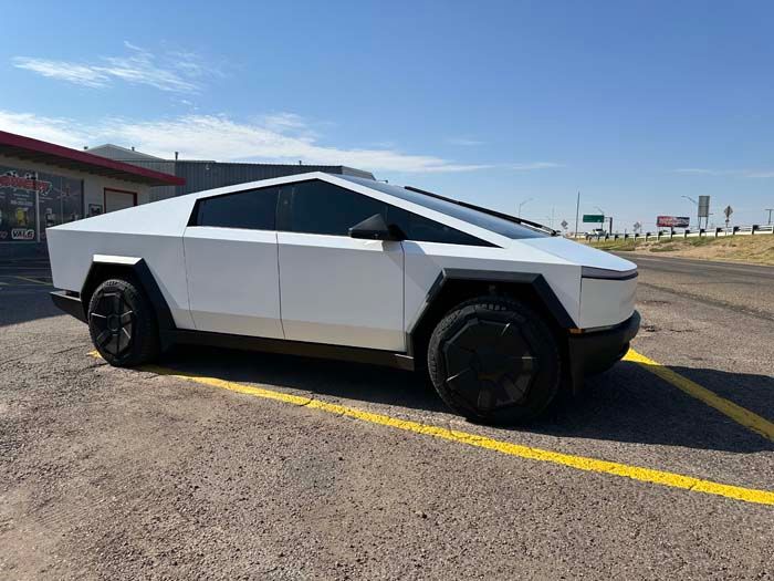 White Tesla Cybertruck parked on asphalt next to a building on a sunny day.