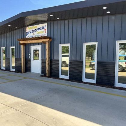 Daycare building with dark gray metal siding, white windows, and a wooden entrance.