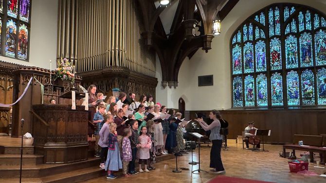 Children’s choir performing in a church sanctuary, with stained glass windows and an organ backdrop