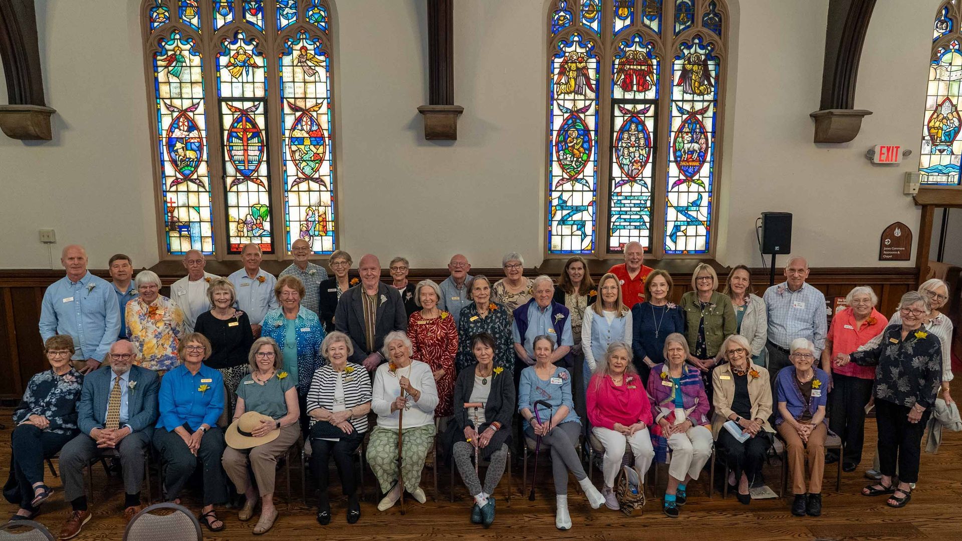 Large group posing for a photo inside a church, with stained glass windows and rows of seated people.