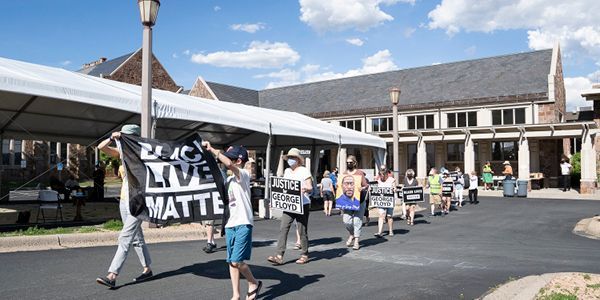 Protesters marching with signs, including a large “LIVES MATTER” banner, outside a building.