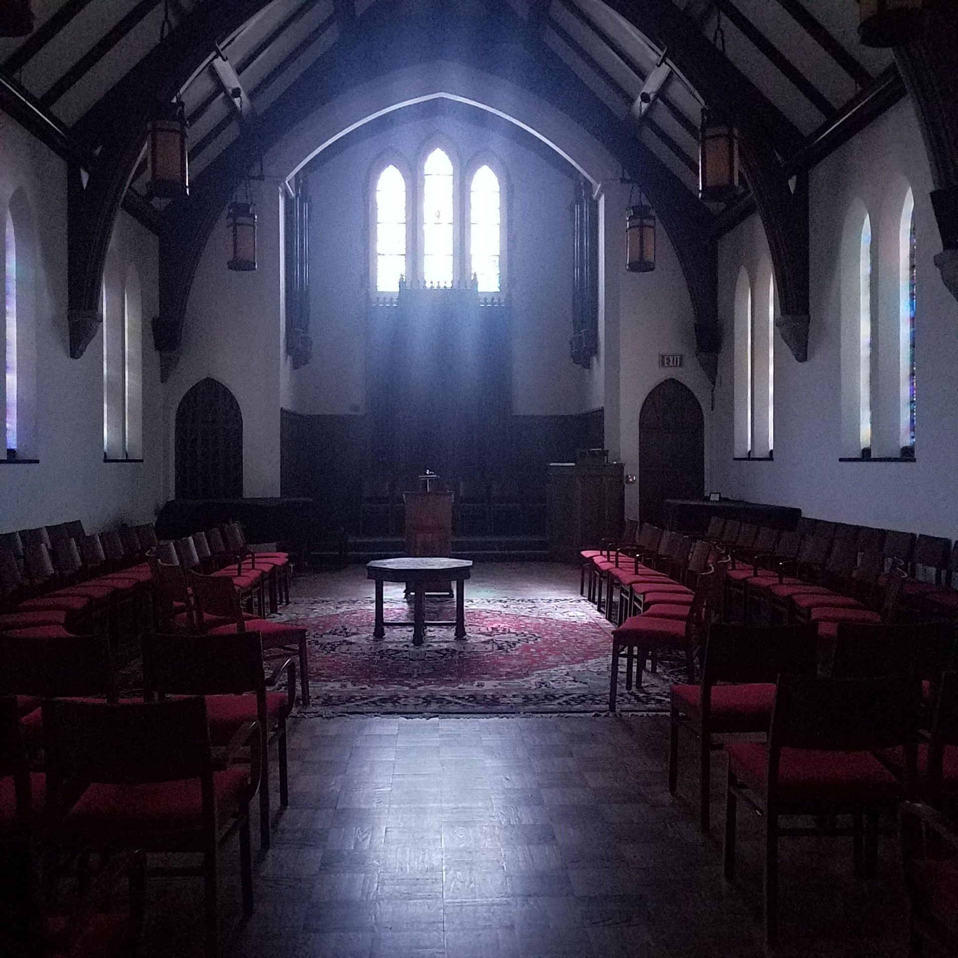 Dim church interior with rows of chairs, central altar, and light from tall arched windows