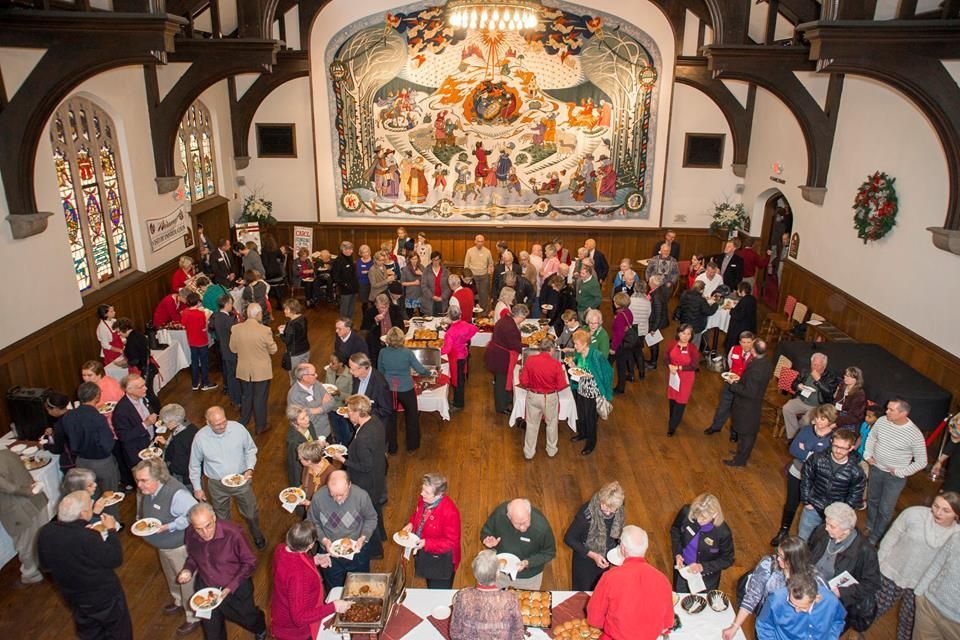 Crowded hall with people mingling beneath a large mural, festive holiday gathering