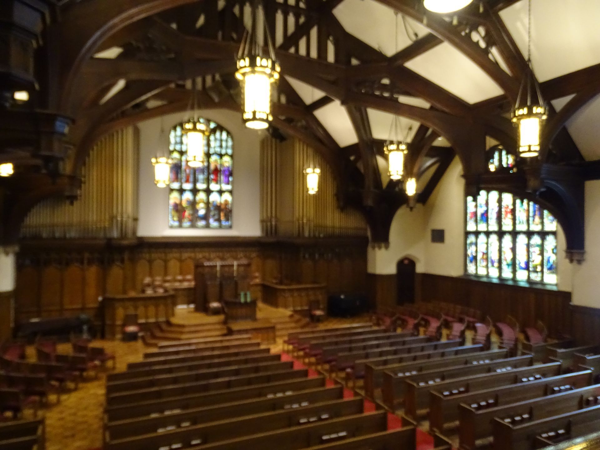 Wood-paneled church hall with stained-glass windows and rows of pews facing a raised pulpit