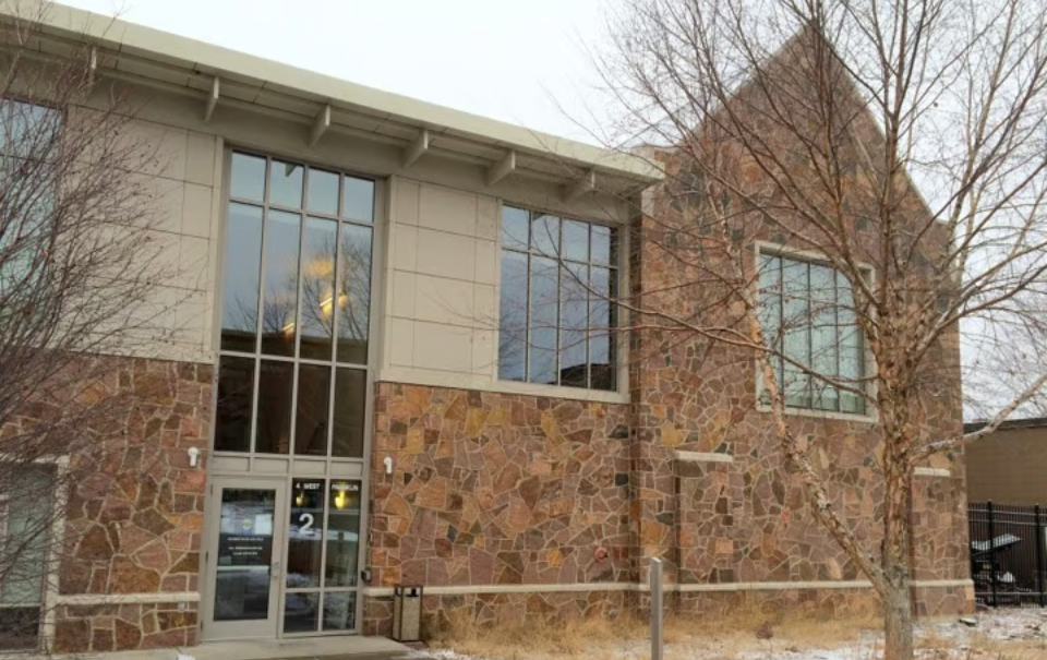 Brick and stone building facade with large windows and a glass entrance under bare winter trees