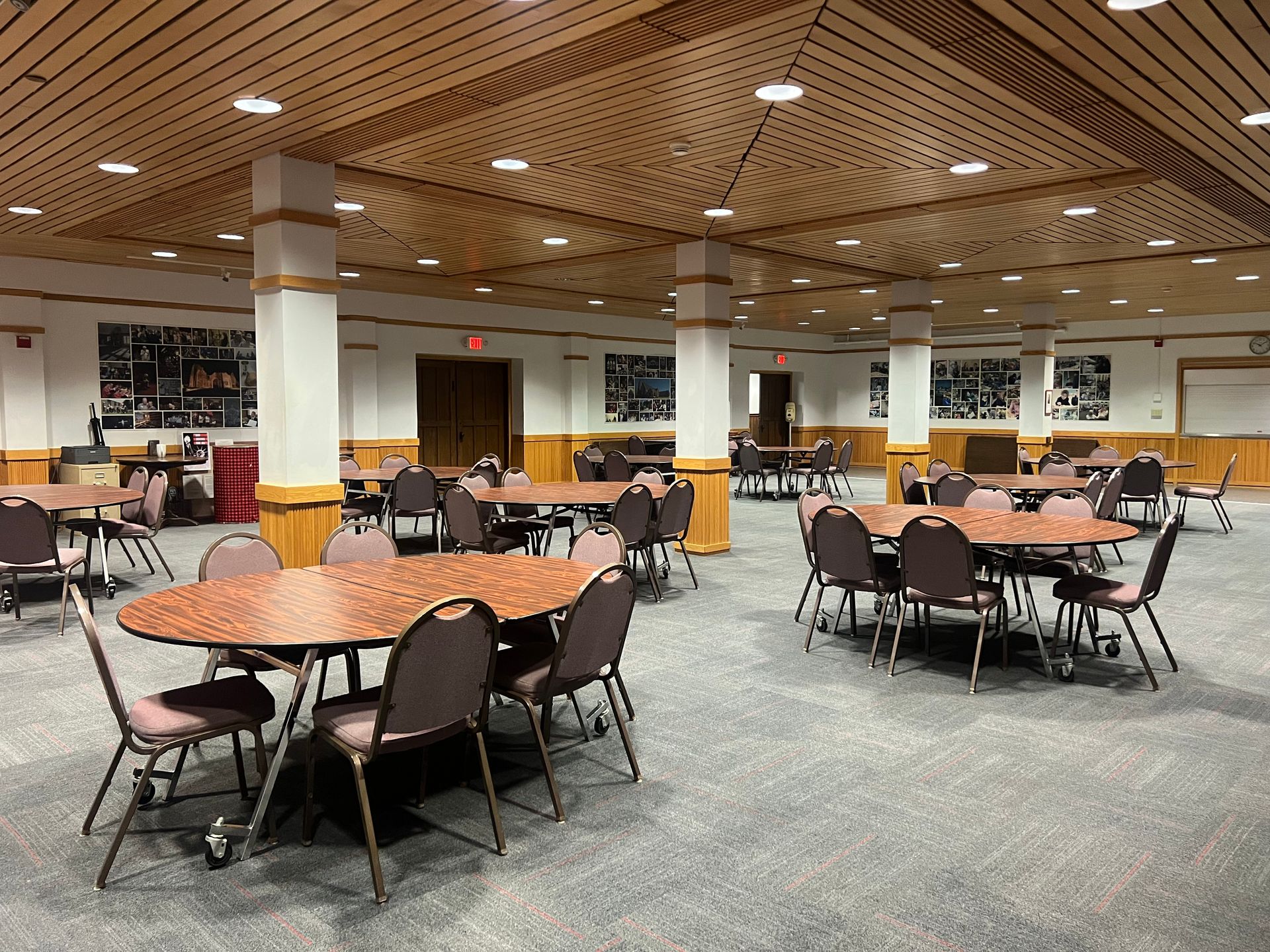 Large empty banquet hall with round tables, brown chairs, and a patterned wooden ceiling