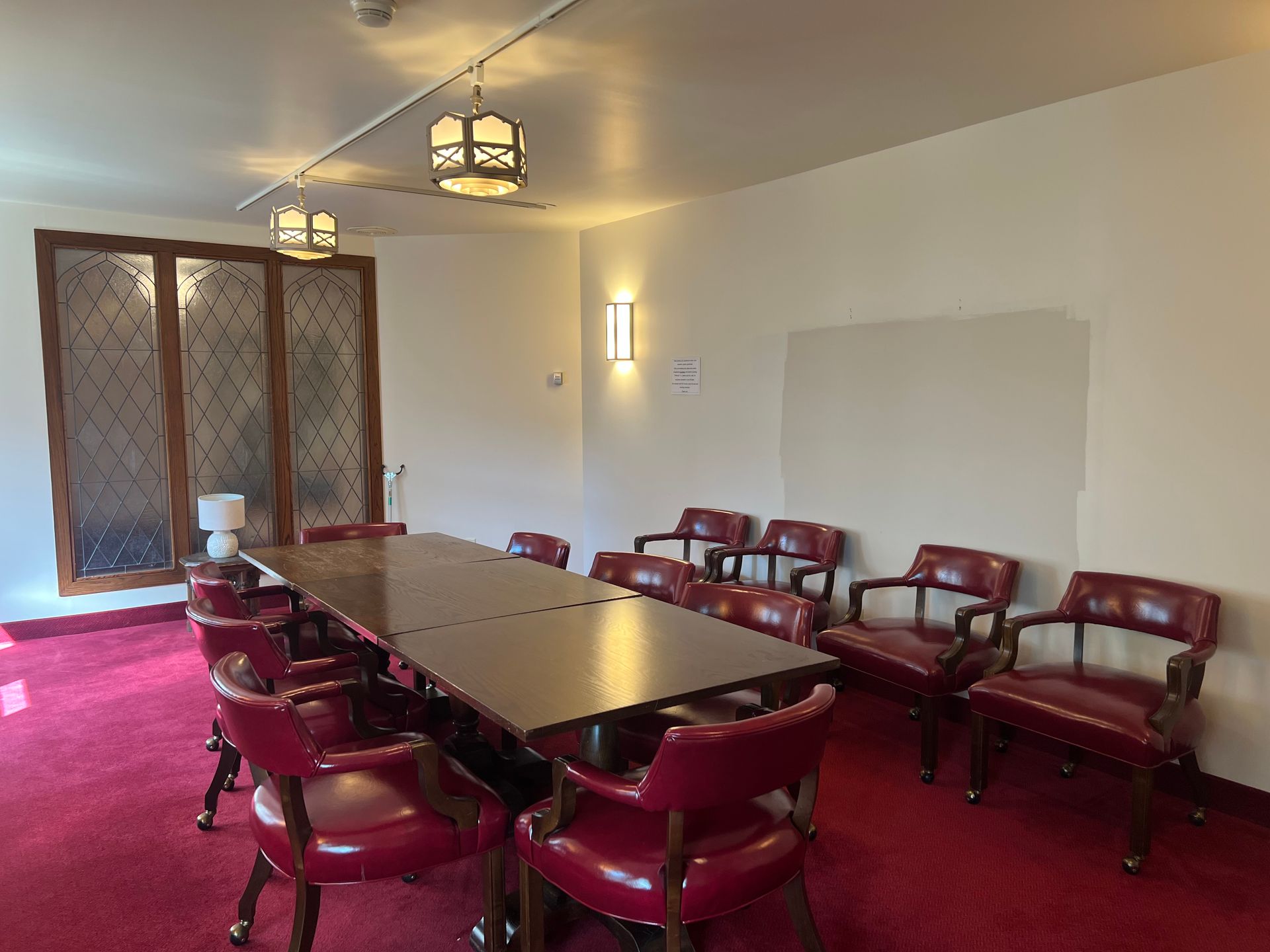 Conference room with red chairs around a long table, carpeted floor, and windows along one wall.