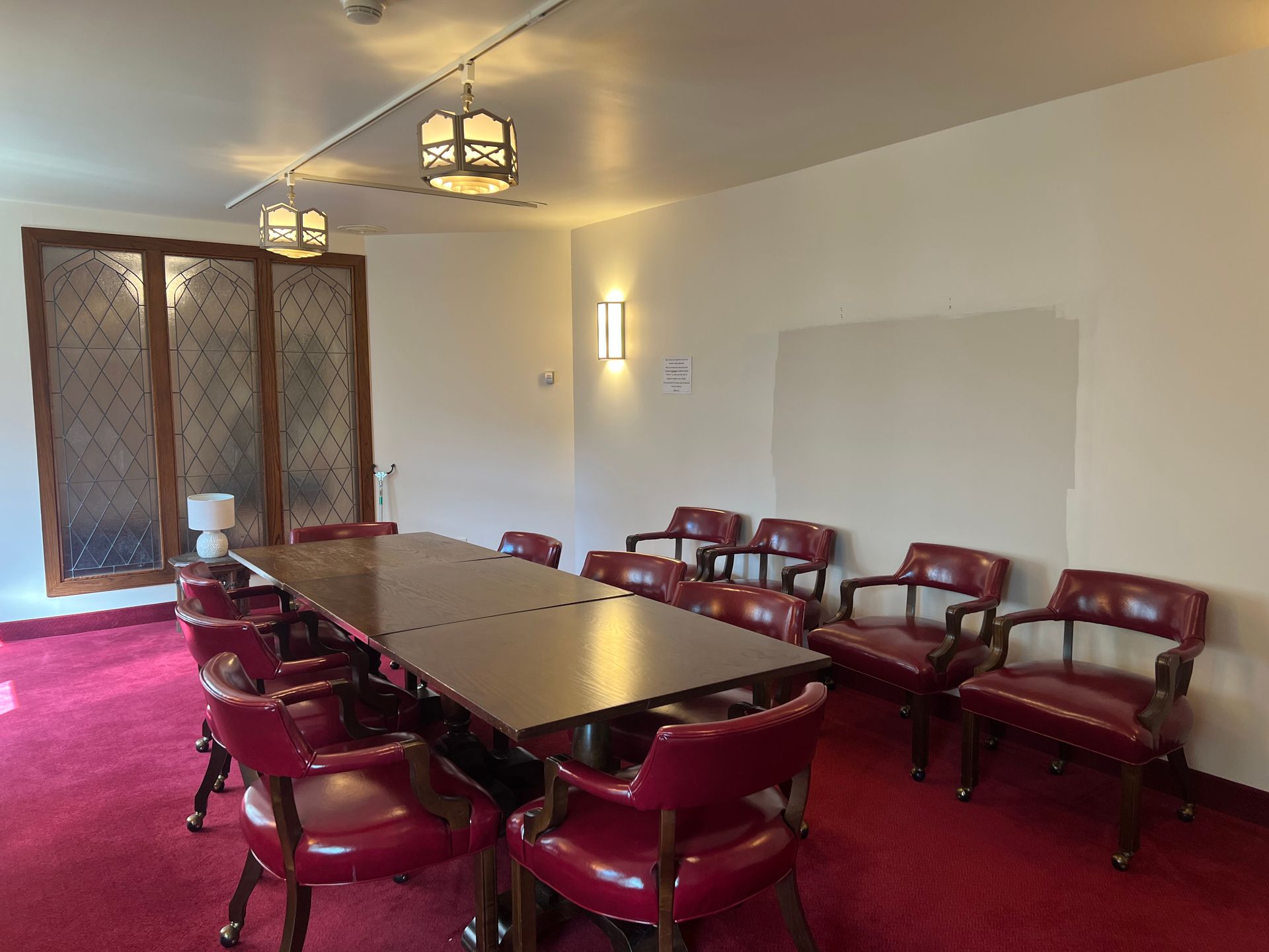 Conference room with red chairs around a long table, red carpet, and wall lights.