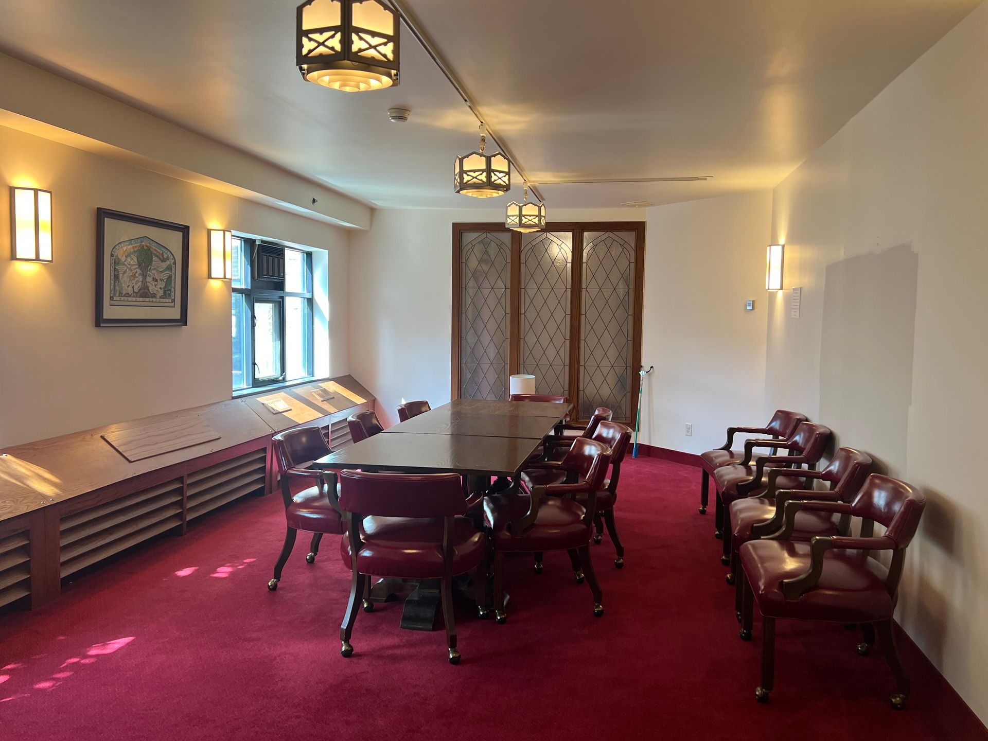 Conference room with red carpet, wooden table, chairs, and wall sconces