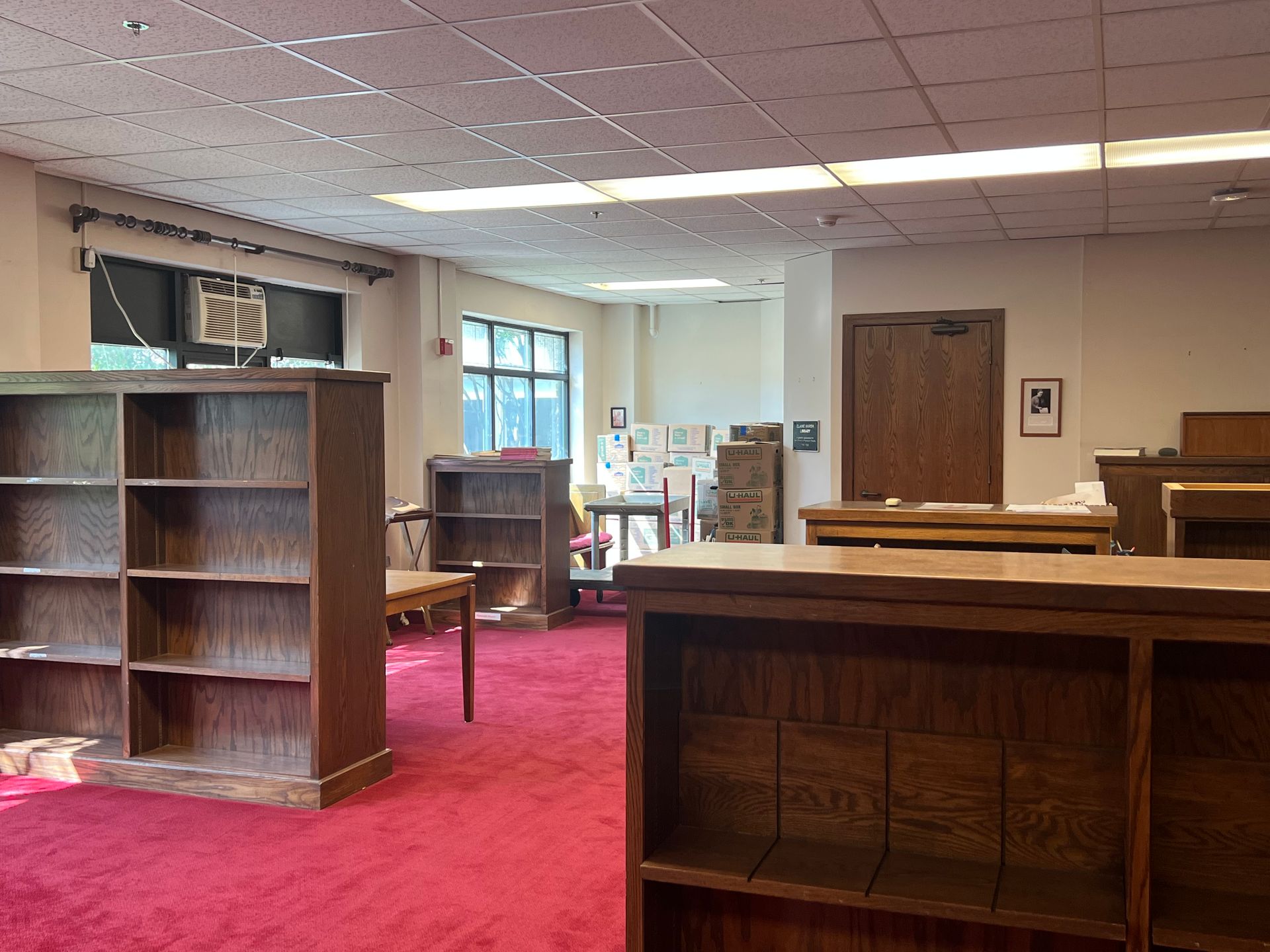 Empty library room with red carpet, wooden bookshelves, and large windows.