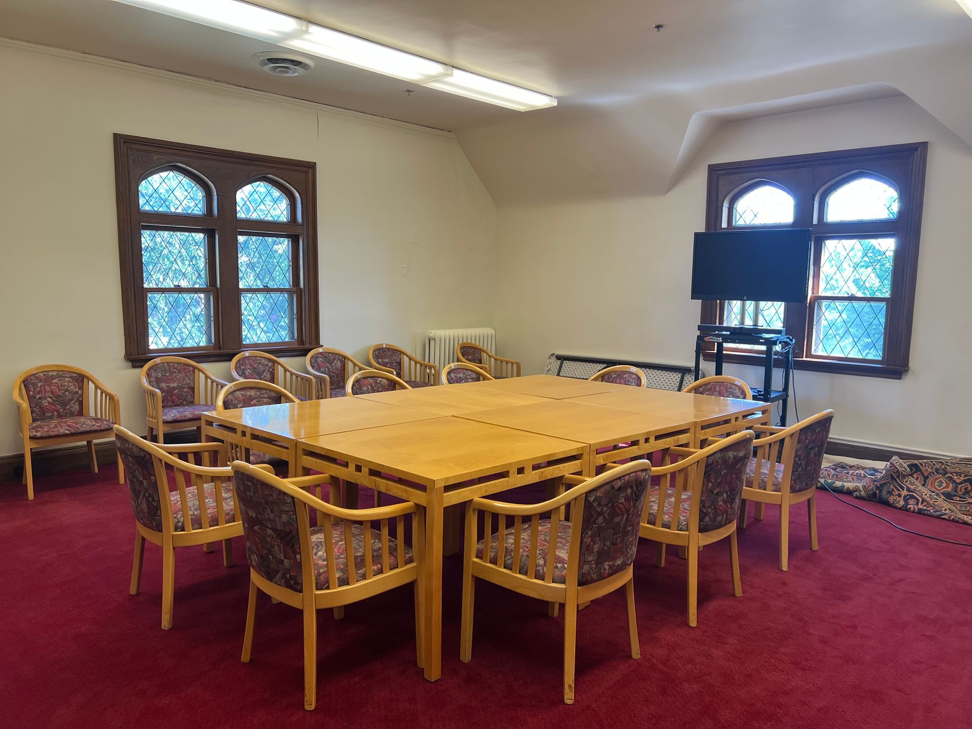 Empty dining room with wooden table set, wicker chairs, maroon carpet, and arched windows