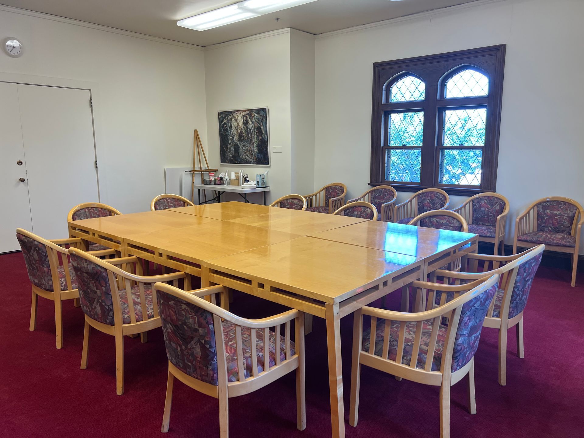 Conference room with a large wooden table, patterned chairs, and a windowed wall.