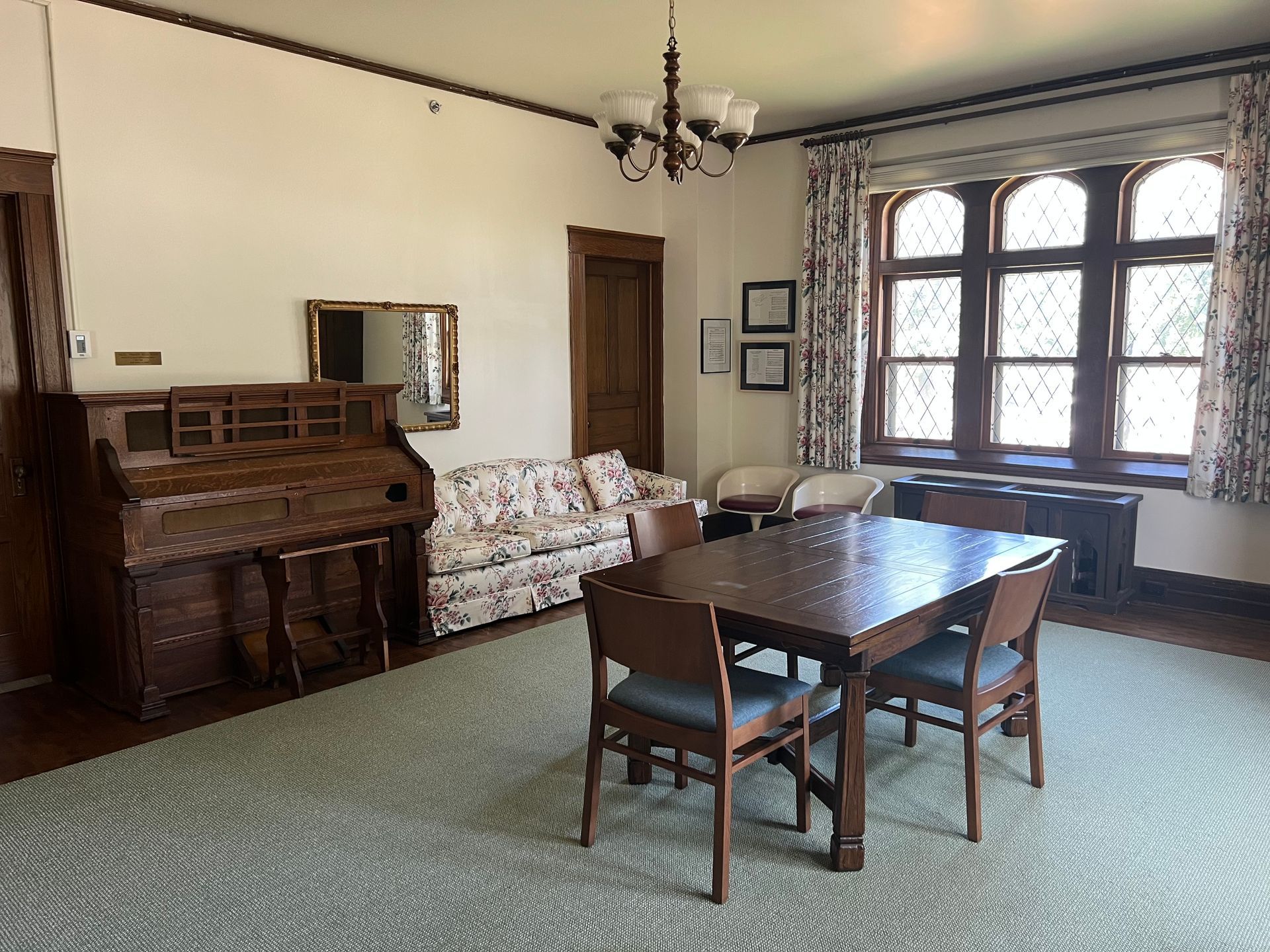 Vintage living room with piano, floral sofa, wooden table, and large window by curtains