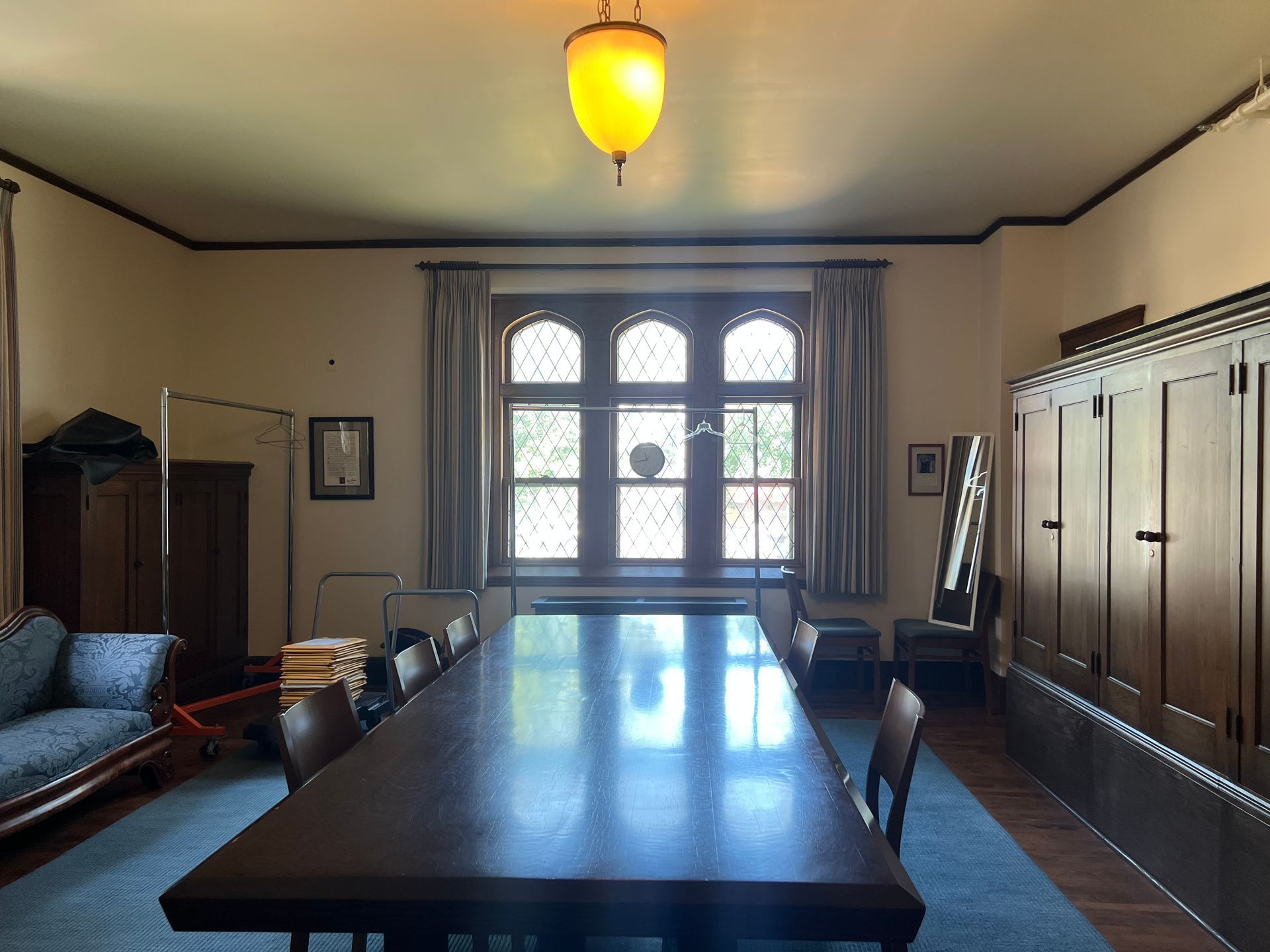 Empty conference room with a long wooden table, cabinets, and a large arched window.