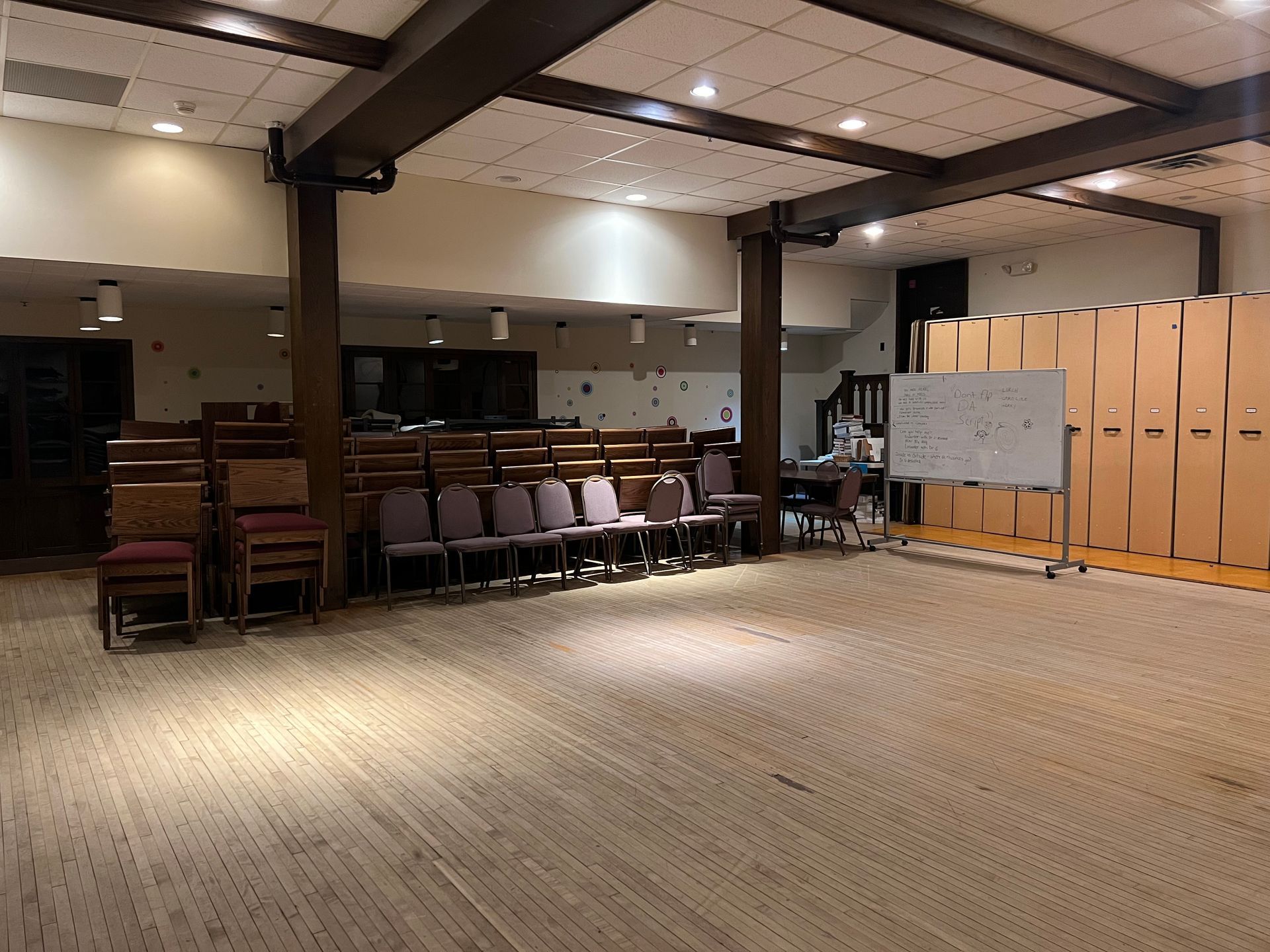 Empty multipurpose hall with stacked chairs, a whiteboard, and beige storage cabinets.