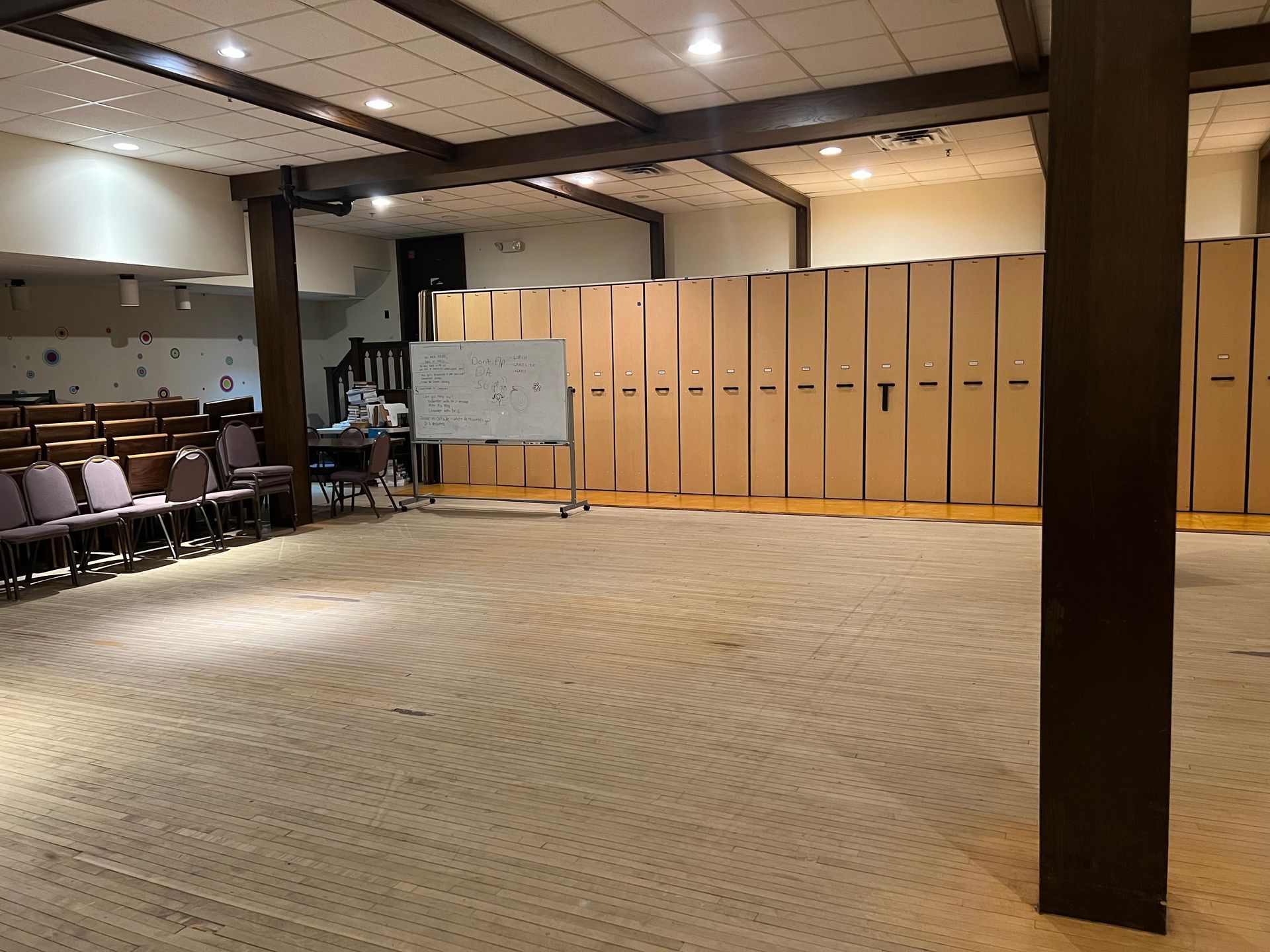 Empty meeting room with stacked chairs, whiteboard, and beige storage cabinets on carpeted floor