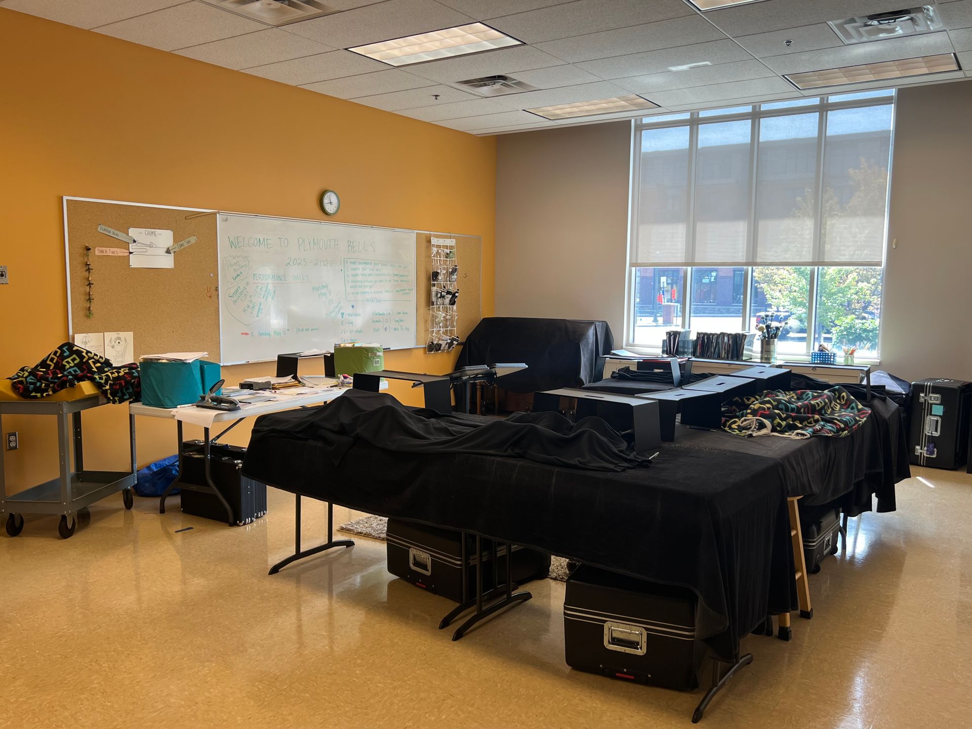 Classroom with tables covered in black cloth, computers, whiteboard, and large windows.