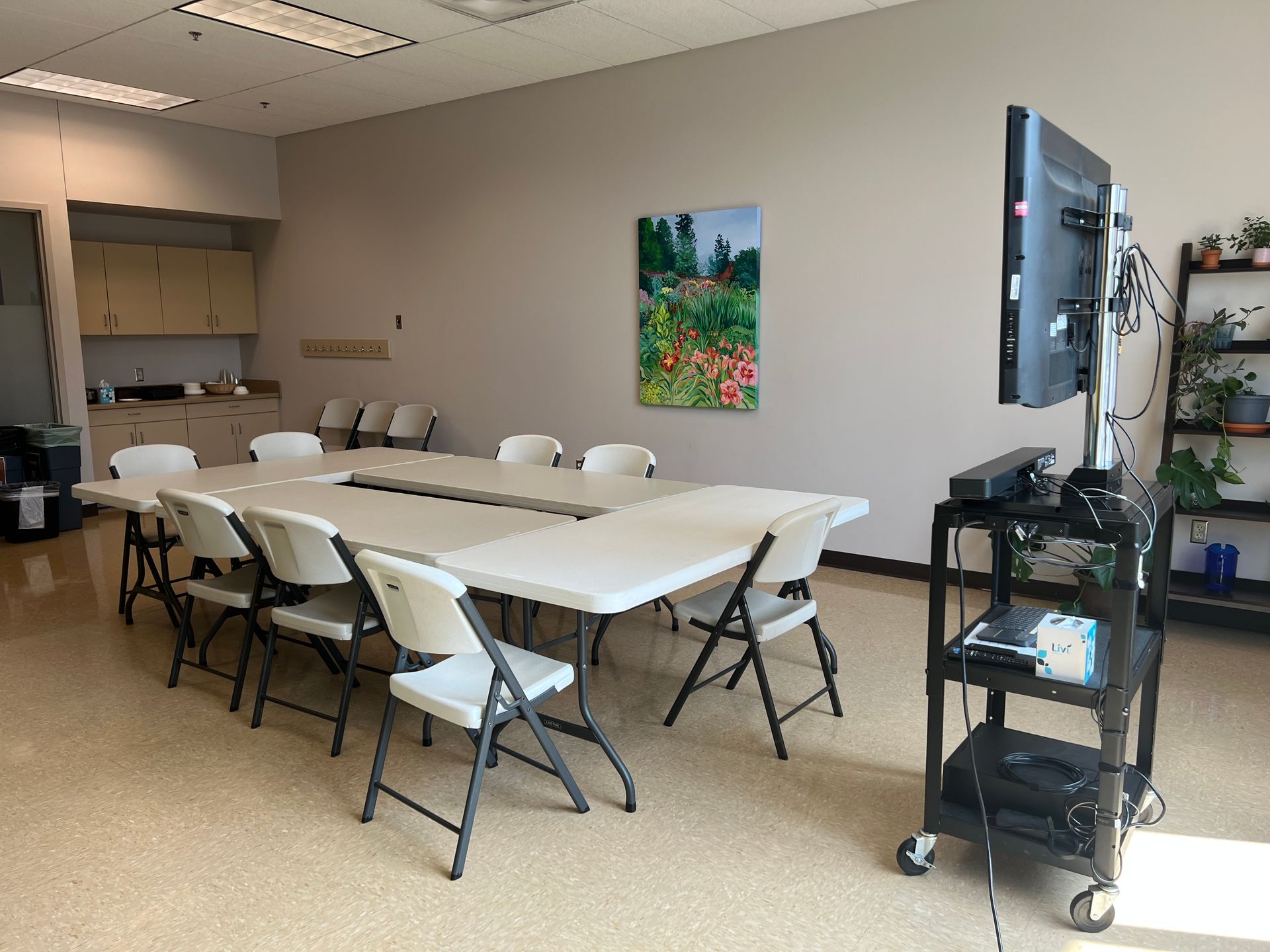 Conference room with a long white table, folding chairs, wall art, and a TV on a rolling stand