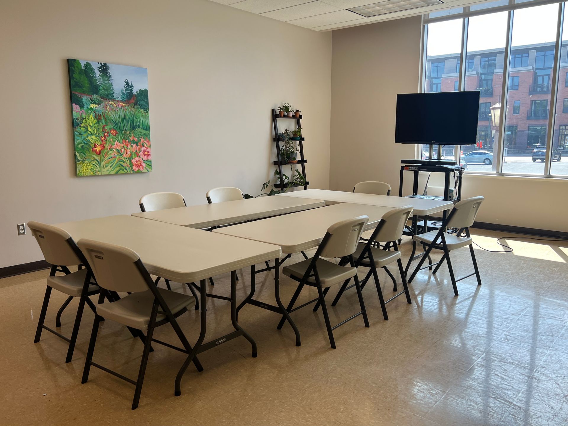 Conference room with a long table, folding chairs, TV screen, and large window.