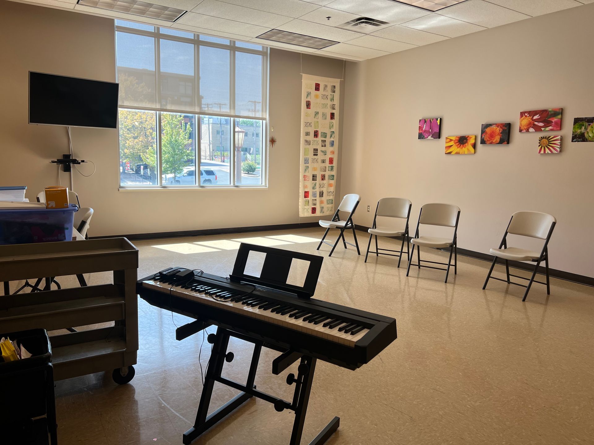 Empty classroom with a keyboard, chairs, a TV, and large windows.