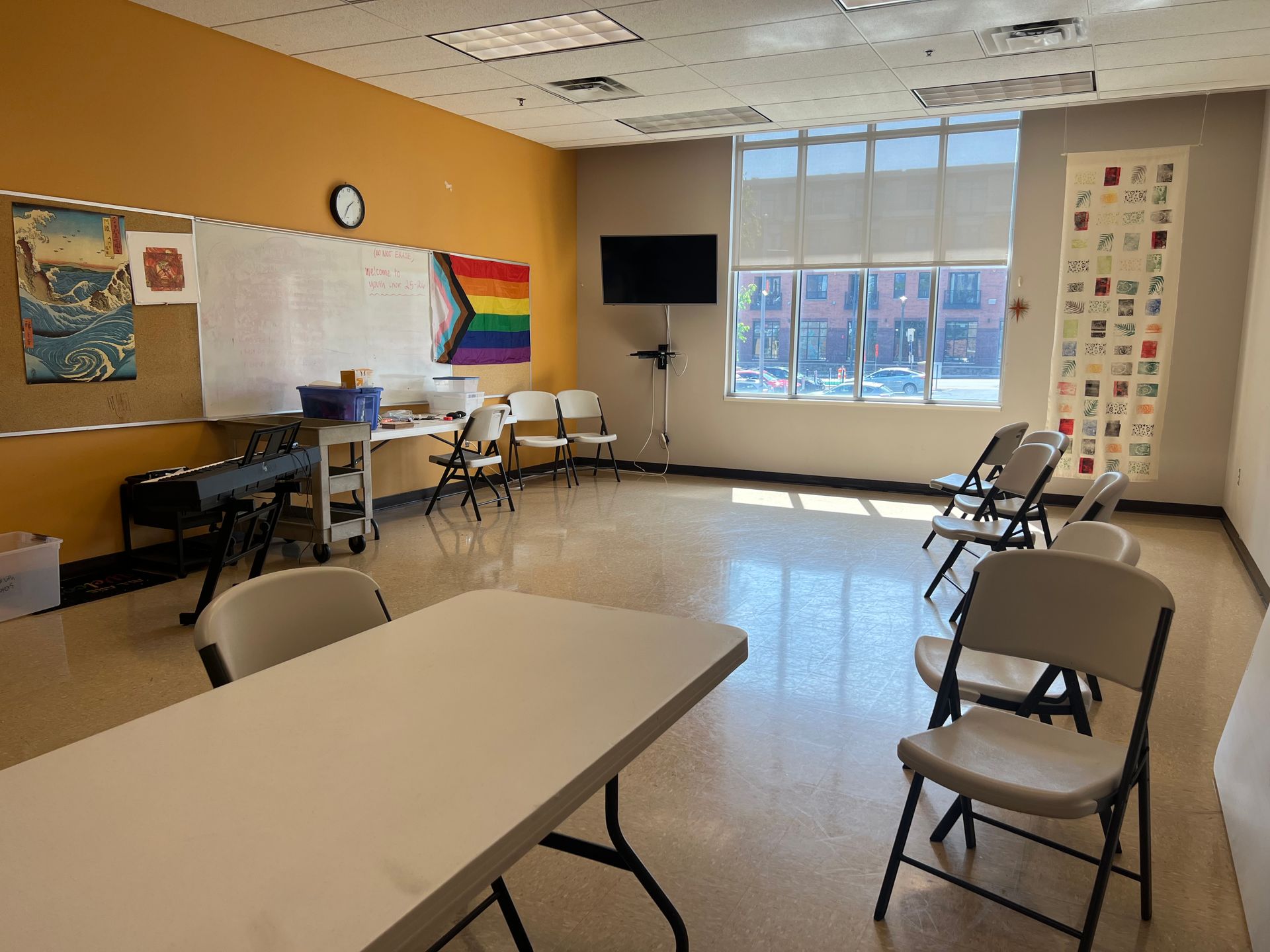 Empty classroom with tables, chairs, whiteboard, wall posters, and a large window.