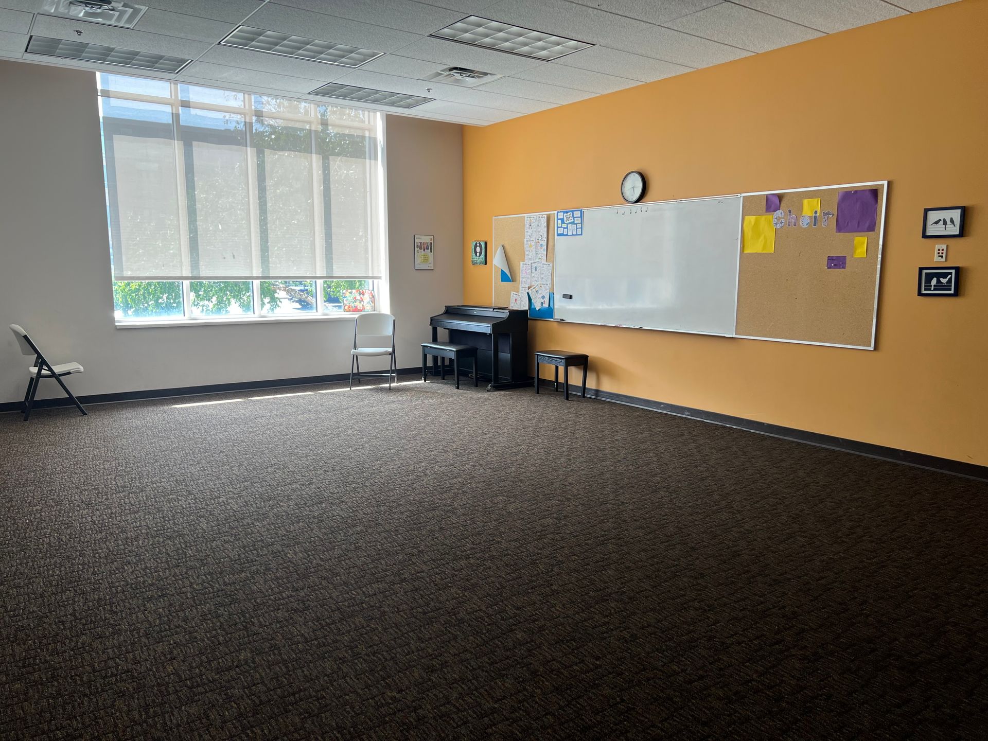 Empty classroom with carpet, large windows, whiteboard, and bulletin board on a tan wall