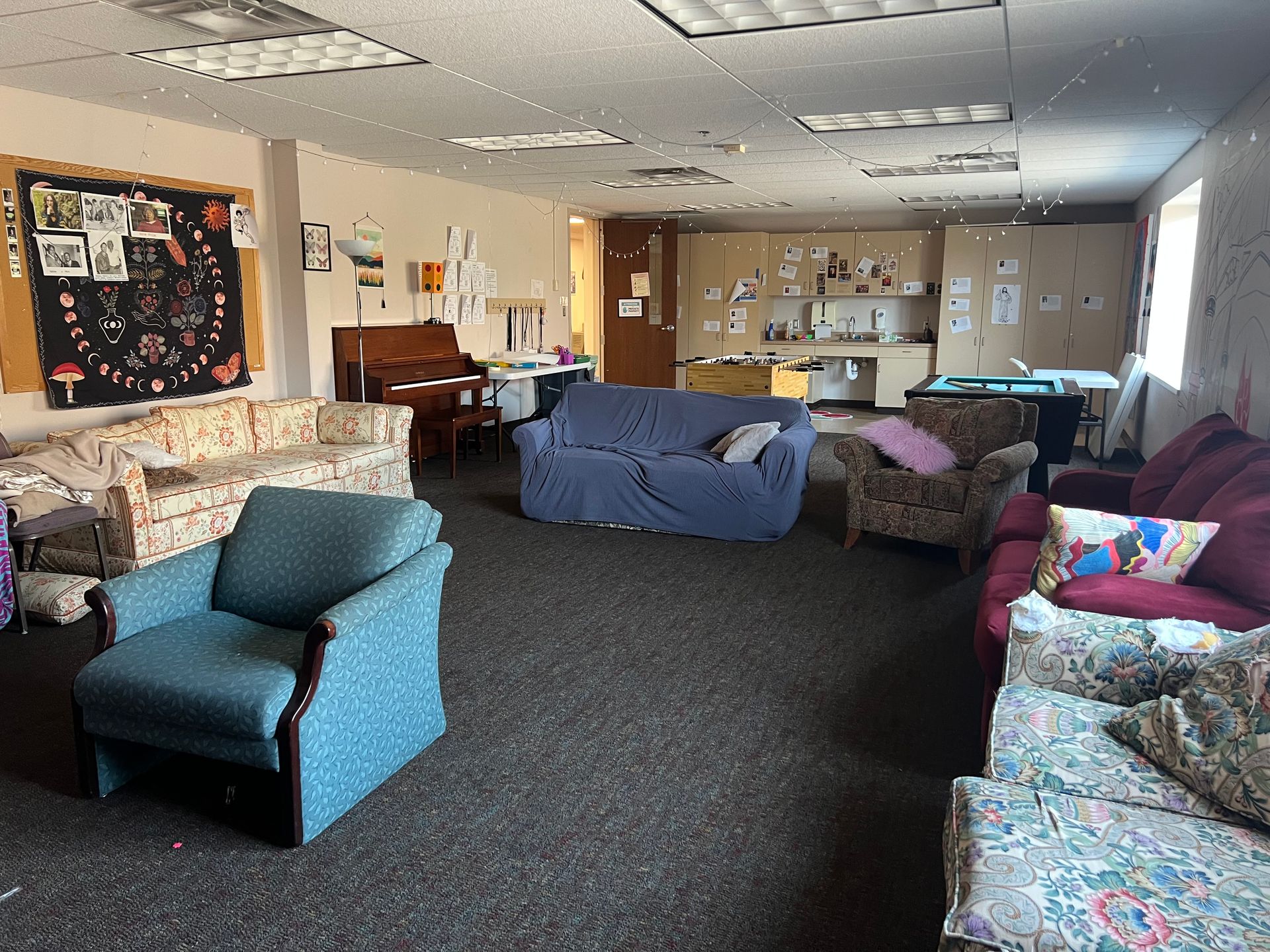 Cozy lounge with patterned armchairs, blue sofas, and a carpeted floor under fluorescent ceiling lights.