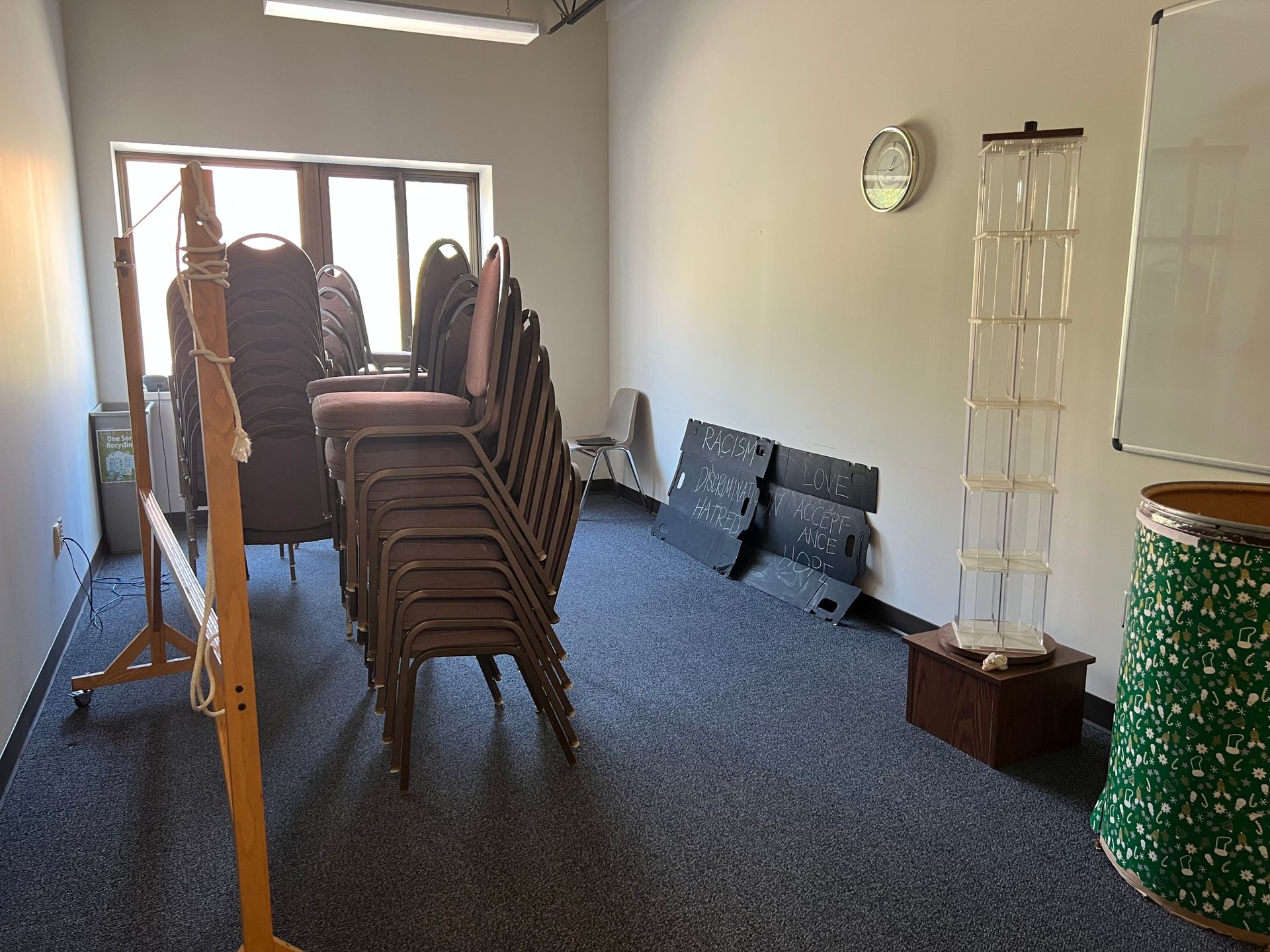 Empty room with stacked chairs, a ladder, a wall clock, and a green podium on blue carpet.