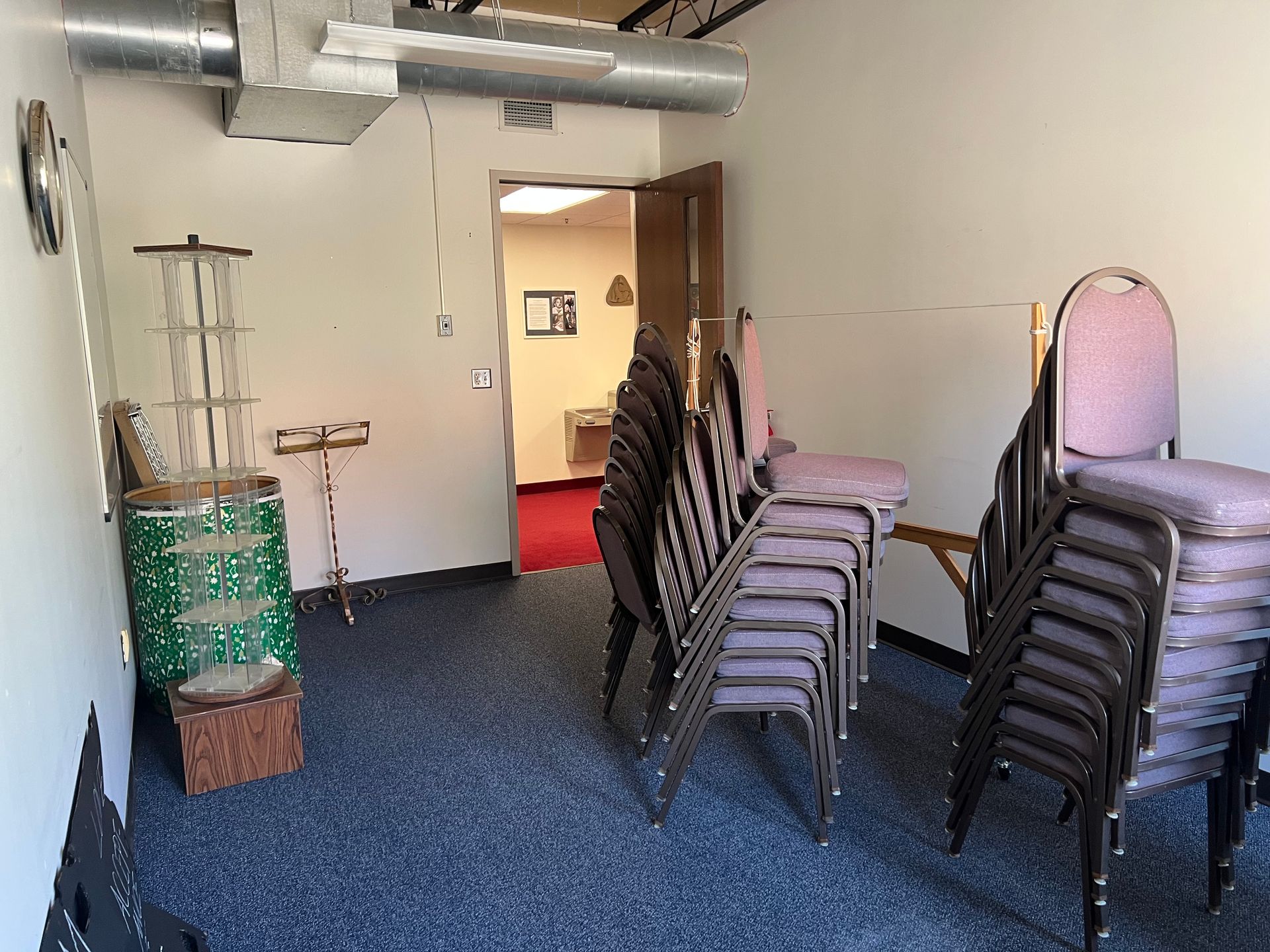 Empty event room with stacked chairs, carpeted floor, and exposed ductwork.