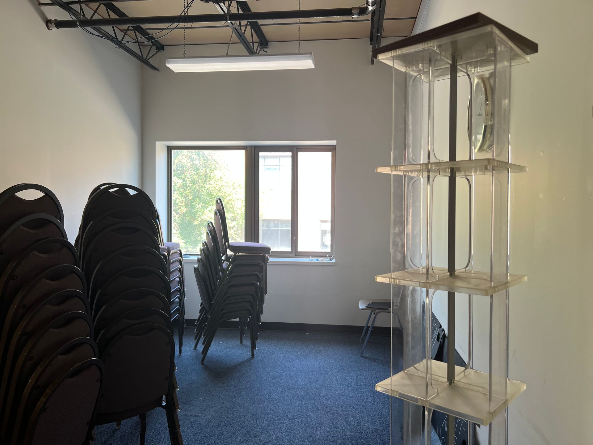 Storage room with stacked black chairs, a window, and a tall white shelving unit on the right.
