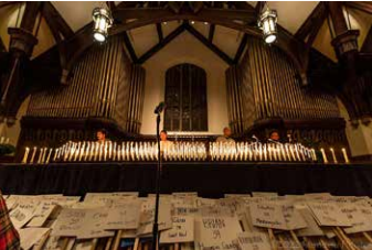 Choir singing in a church beneath organ pipes, with sheet music spread across the foreground
