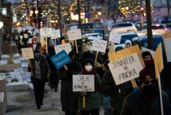 Protesters marching with signs on a city street at dusk, including one reading “JACK W HINKA” and another “SUMMER PINKA.”