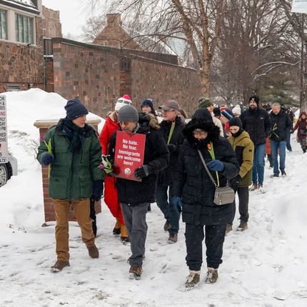 People walking in a snowy outdoor march, one holding a red sign.