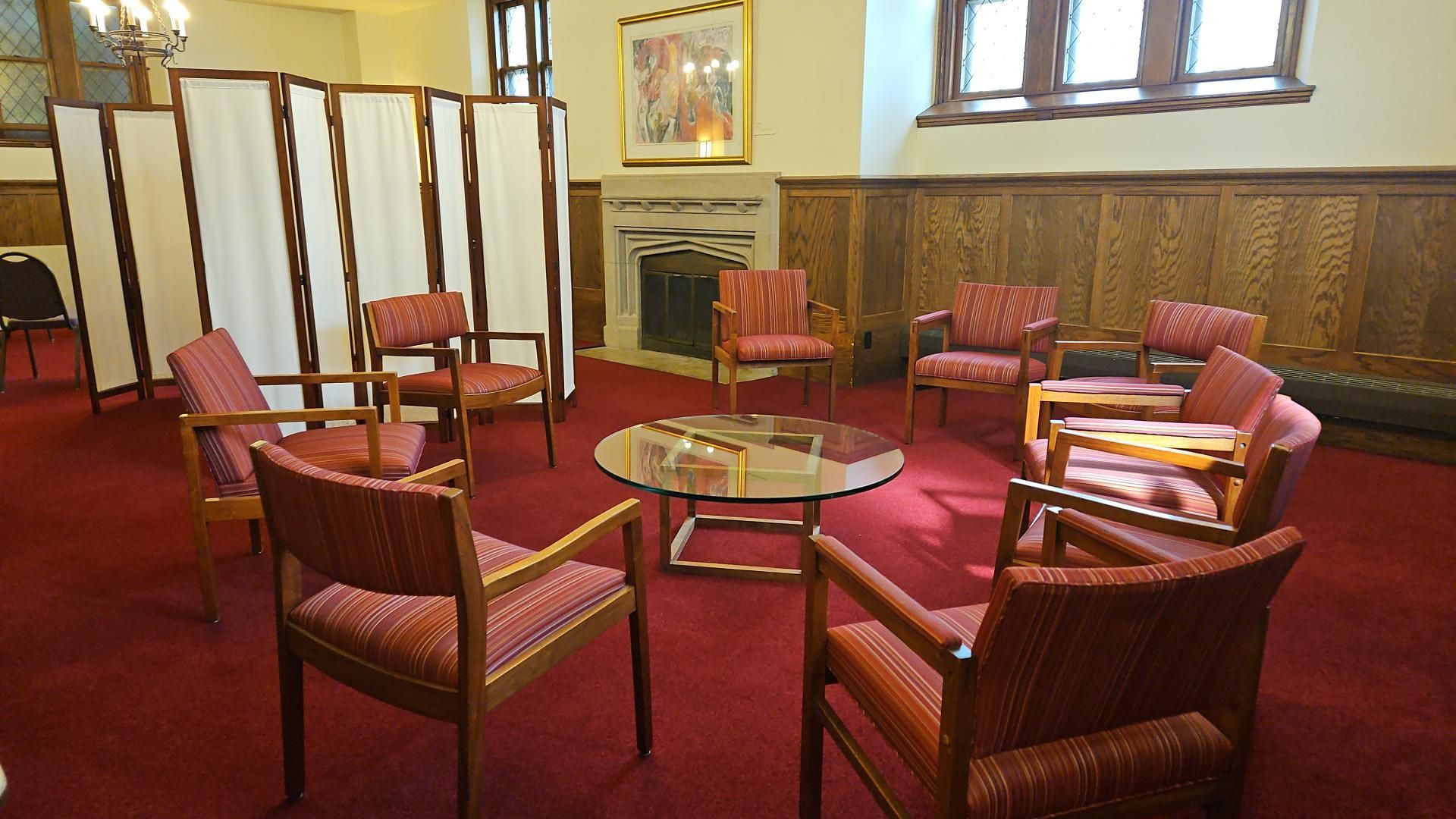 Empty lounge with red chairs around glass tables and a folding screen in a wood-paneled room