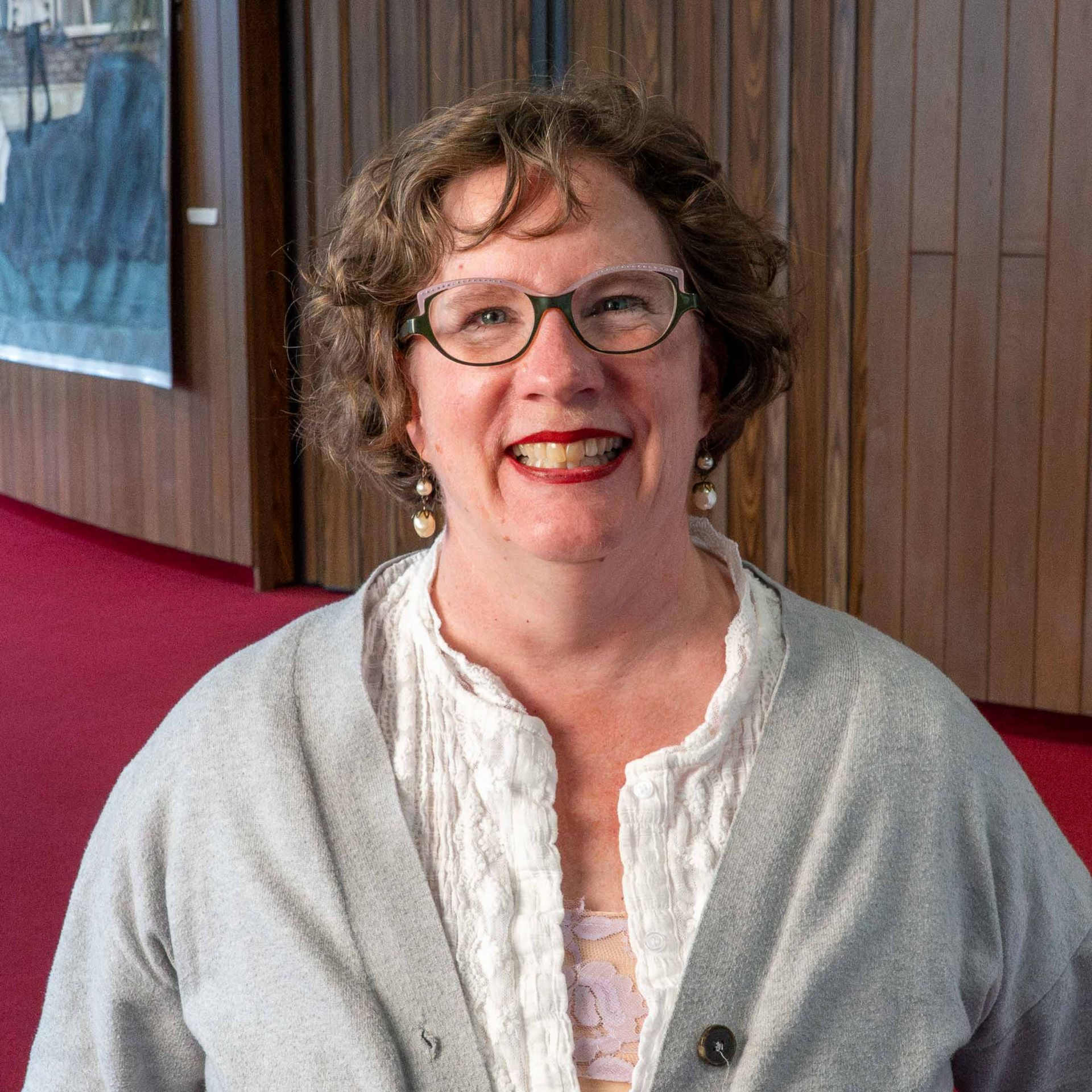 Smiling woman in glasses and a gray shawl standing indoors on a red carpet
